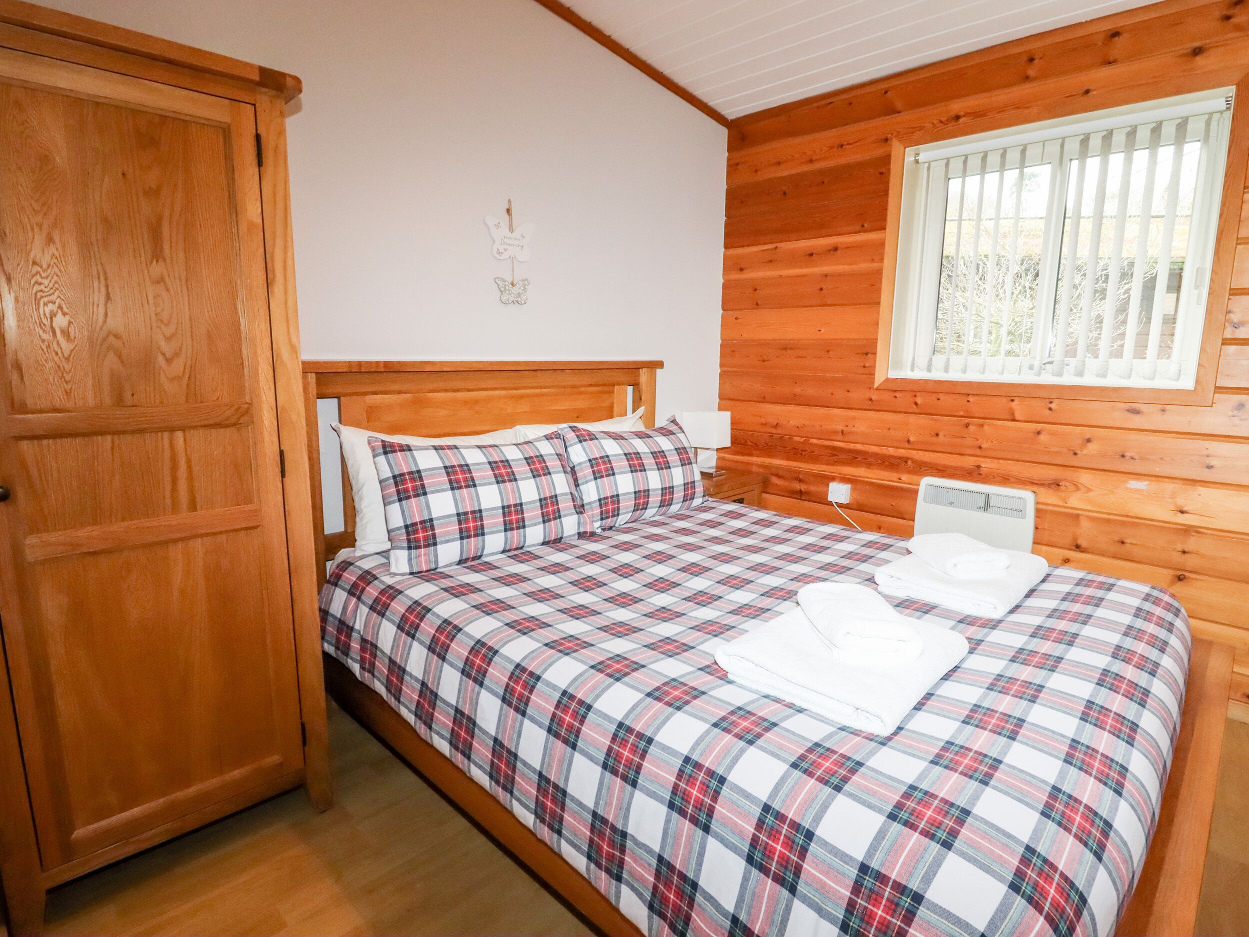 A bedroom with a wooden bed, a nightstand, a window with blinds, and a wardrobe.