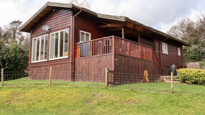 Una cabaña de madera con balcón, ventanas amplias y un patio cercado.