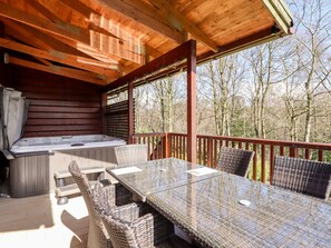 A covered outdoor area with a hot tub, wicker furniture, and a view of trees. - Watersview Lodge (Leek)