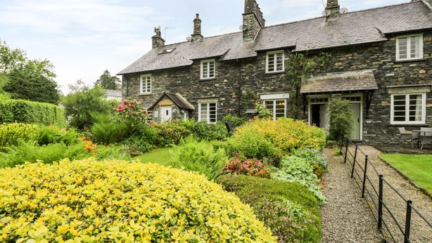 A stone building with multiple windows and a garden with yellow flowers.