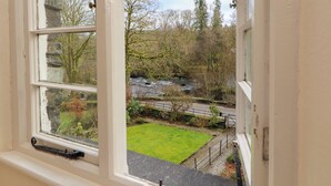 A view through a window of a stone building with a grassy yard and a stream.