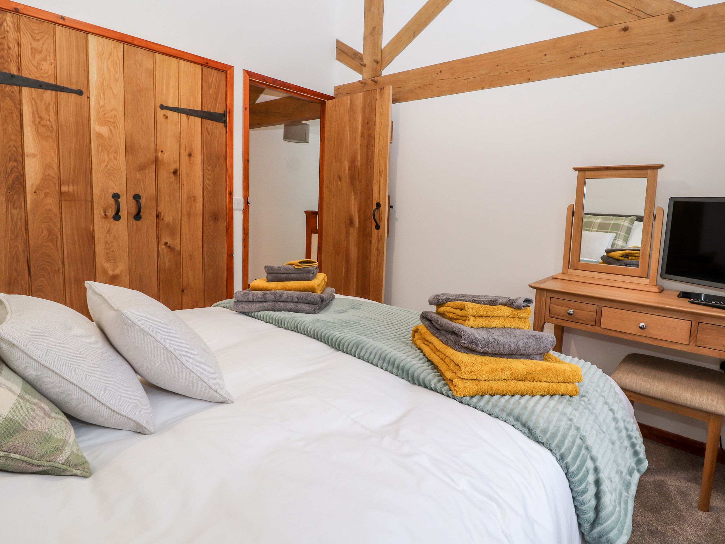 Un dormitorio con cama, armario de madera, cómoda, espejo y televisión.