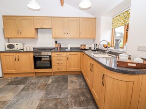 A modern kitchen with wooden cabinets, a built-in oven, a microwave, and a sink. - The Old Cart House (Oswestry)