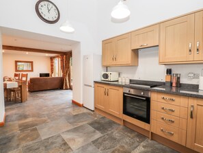 A modern kitchen with wooden cabinets, a built-in oven, and a microwave. - The Old Cart House (Oswestry)
