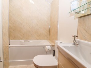 A bathroom with a bathtub, toilet, and a glass shelf with toiletries. - The Old Cart House (Oswestry)