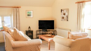 A living room with beige sofas, a TV, a fireplace, and artwork on the walls. - Stiperstones View (Shrewsbury)