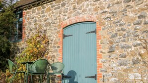 A stone building with a blue door, a window, and a small outdoor seating area with chairs. - Stiperstones View (Shrewsbury)