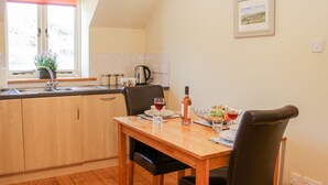 A dining area with a wooden table, black chairs, a window with a view, and a kitchen in the background. - Stiperstones View (Shrewsbury)