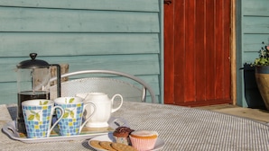 A table set with a teapot, cups, and a muffin on a metal table outside a cottage with a wooden door and a sign reading "Cranberry Cottage". - Cranberry Cottage (Shrewsbury)