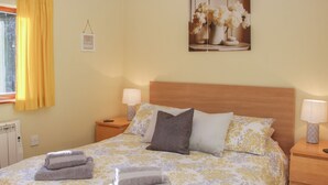 A neatly made bed with floral bedding, two bedside lamps, and a framed picture above the headboard. - Cranberry Cottage (Shrewsbury)