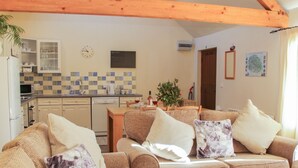 A cozy living room with a sofa, a coffee table, and a dining area with a table and chairs. There is a kitchen in the background with a microwave, a kettle, and a sink. - Cranberry Cottage (Shrewsbury)