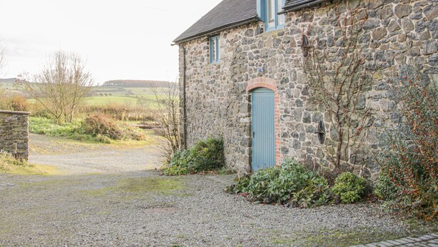 A stone building with a blue door and a gravel driveway. - Cranberry Cottage (Shrewsbury)
