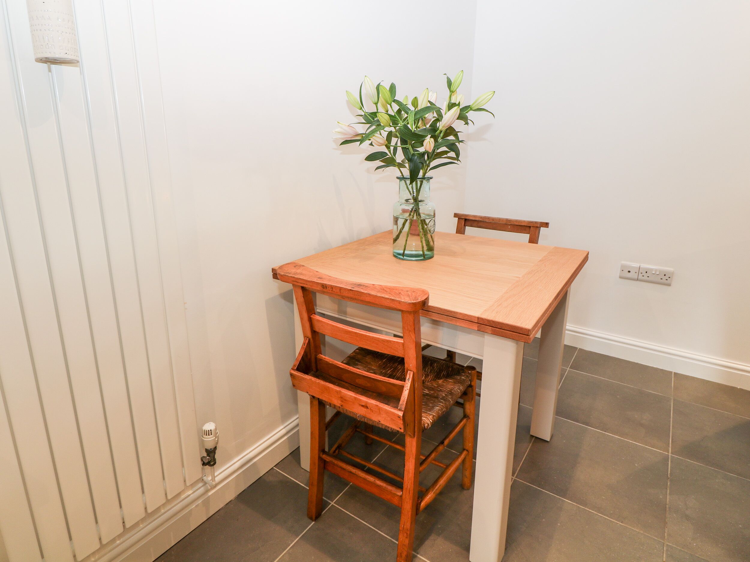 Une petite table à manger avec un vase de fleurs, une chaise et un radiateur.