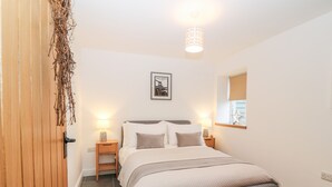 Ein Schlafzimmer mit Bett, Nachttischen, einer Lampe, einem gerahmten Bild an der Wand, einem Fenster mit Sterndekoration und einer hängenden Pflanze.
