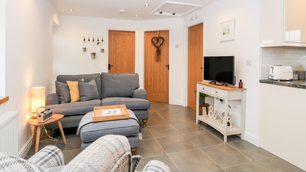 Ein modernes Wohnzimmer mit einem grauen Sofa, einem Fernseher und einer Küchenzeile mit weißen Schränken und einem Toaster.
