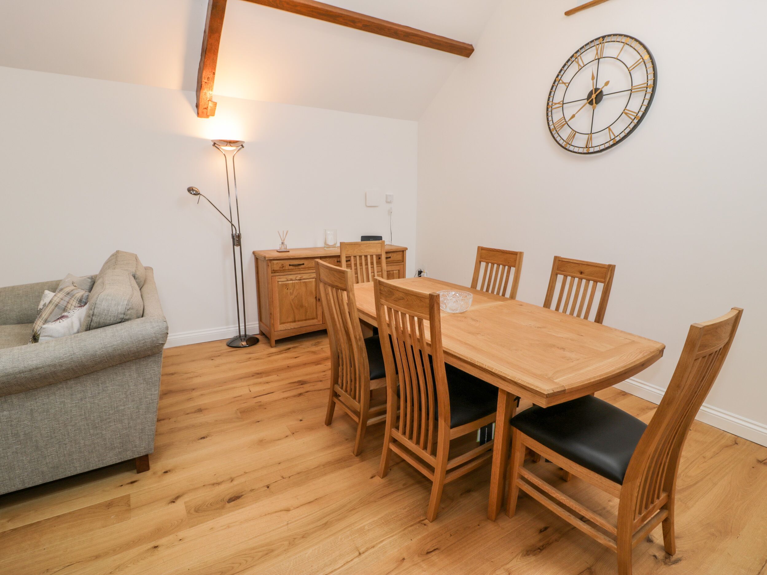 A dining area with a wooden table and chairs, a grey sofa, and a floor lamp.