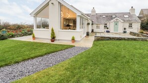 A modern house with a large glass window, a stone pathway, and a well-maintained lawn. - Tŷ'n Lôn Bach (Caernarfon)