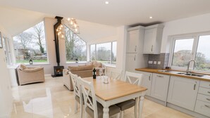 A modern kitchen with white cabinets, a wooden dining table, and a built-in stove. - Tŷ'n Lôn Bach (Caernarfon)