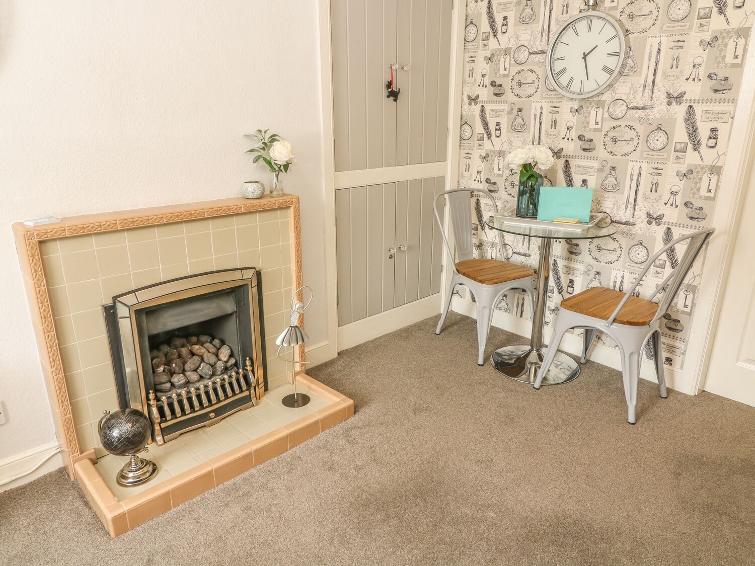 Une pièce avec une cheminée, deux fauteuils, une table et une horloge au mur.