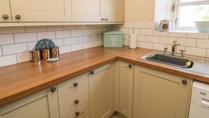 A kitchen with light-colored cabinets, a wooden countertop, a sink, and a window with a view of greenery. - Bank End Cottage (Carnforth)
