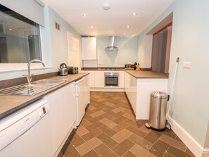 A compact kitchen with white cabinets, a Bosch dishwasher, a stainless steel sink, a microwave, and a trash bin. - Lincoln House (Lincoln)
