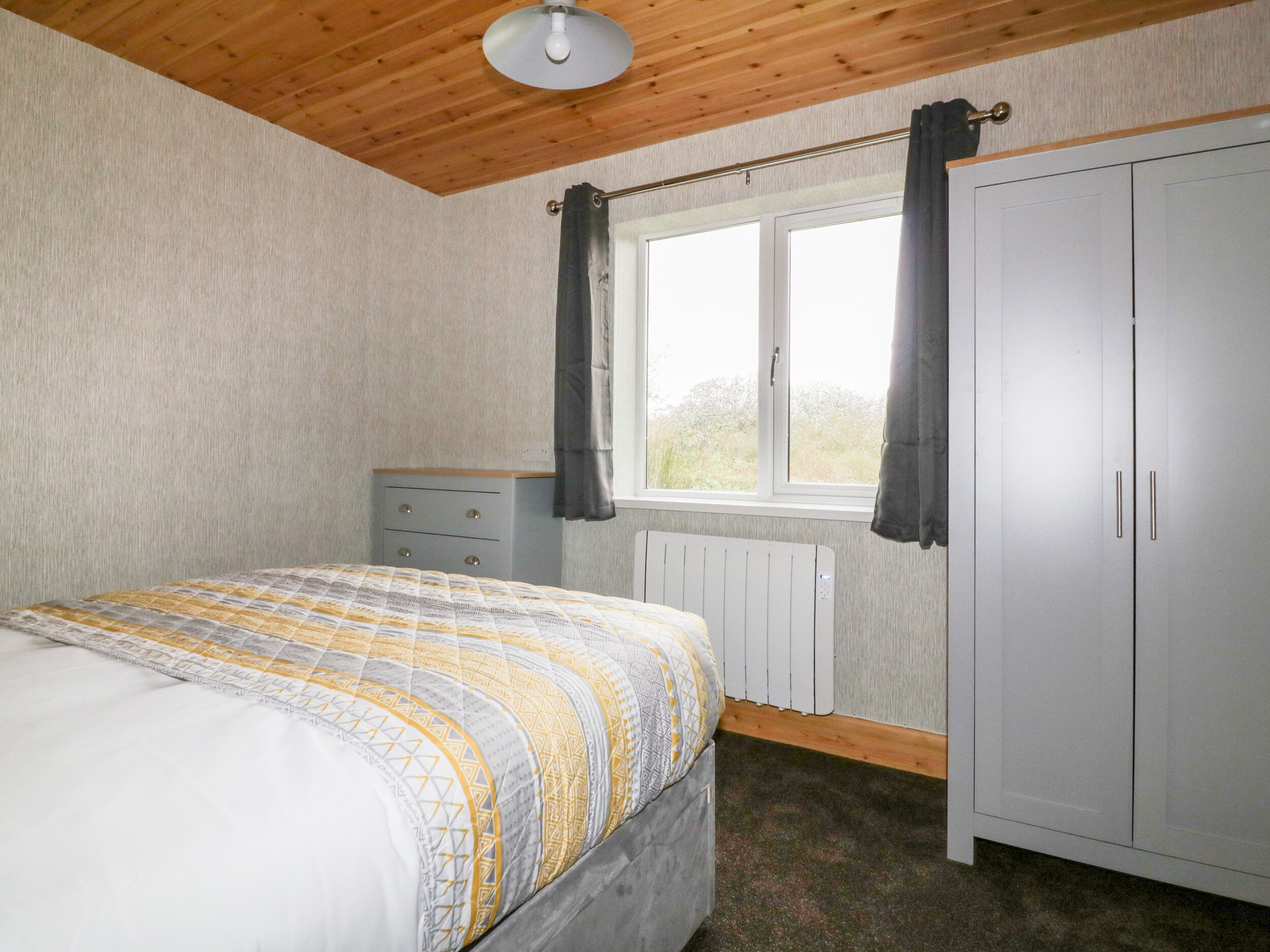A bedroom with a bed, a dresser, a window with curtains, and a radiator.