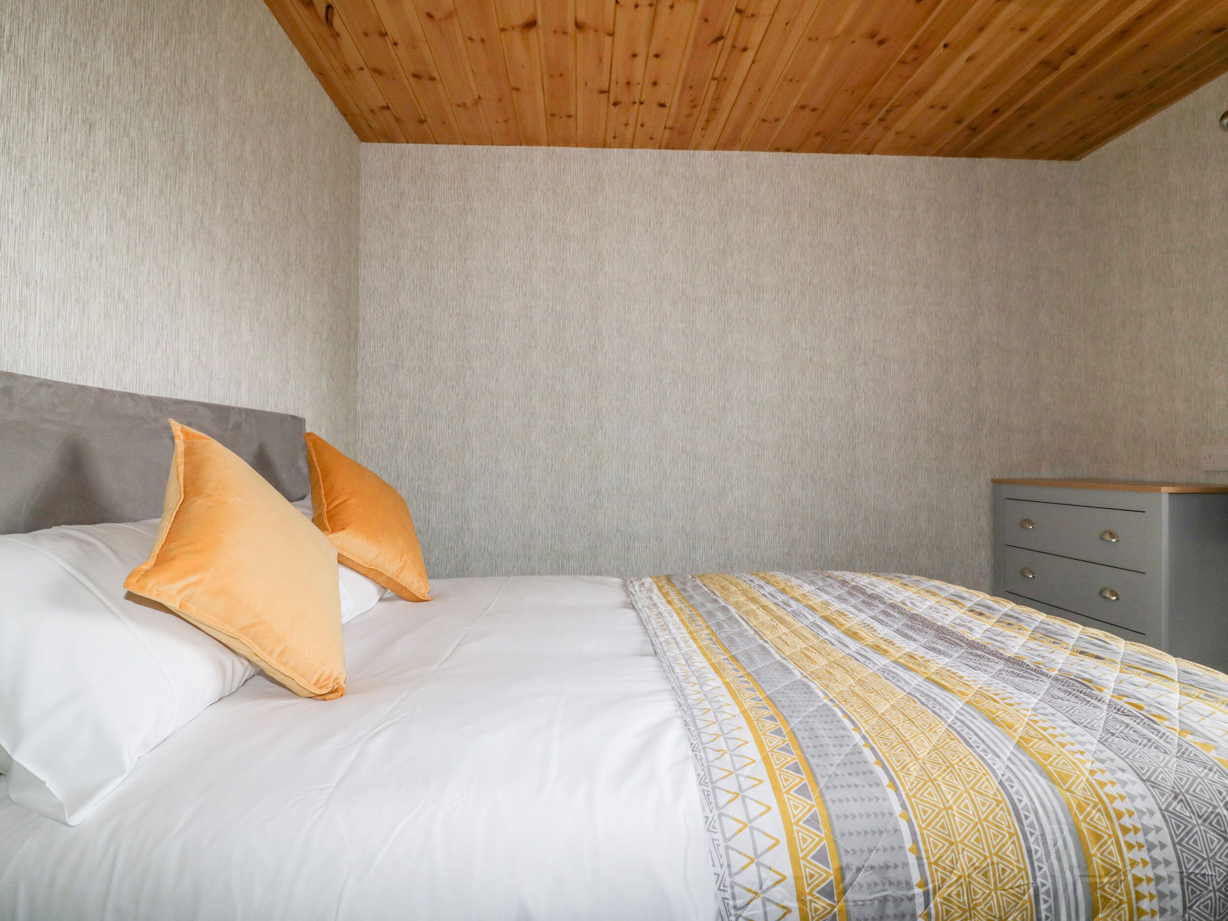 Una camera da letto con un letto, cuscini, una cassettiera e un soffitto in legno.