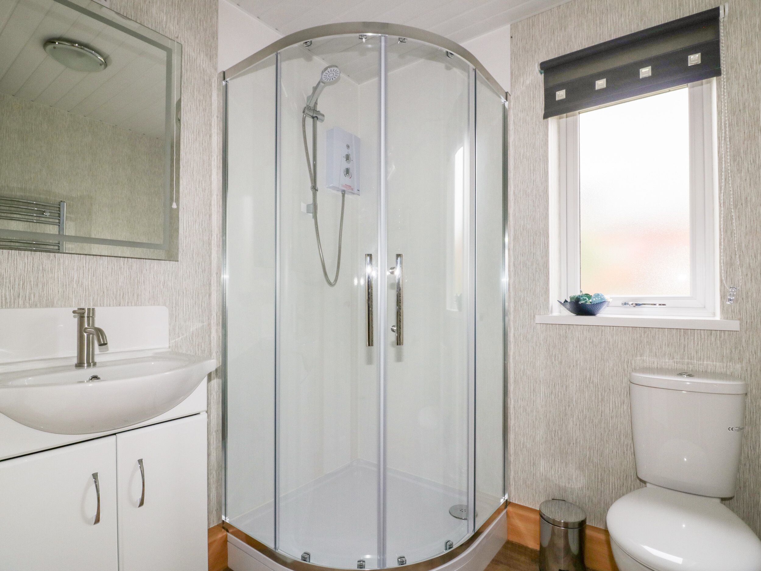 A bathroom with a glass-enclosed shower, a sink, a toilet, and a window.