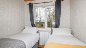 Quarto com duas camas, janela com cortinas e radiador.