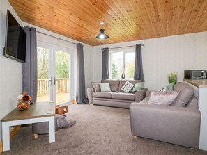 Una sala de estar acogedora con techo de madera, un sofá gris, una mesita con un florero y un microondas sobre la encimera.