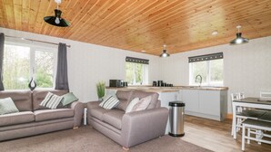 Um interior moderno com teto de madeira, área de cozinha, mesa de jantar e dois sofás.