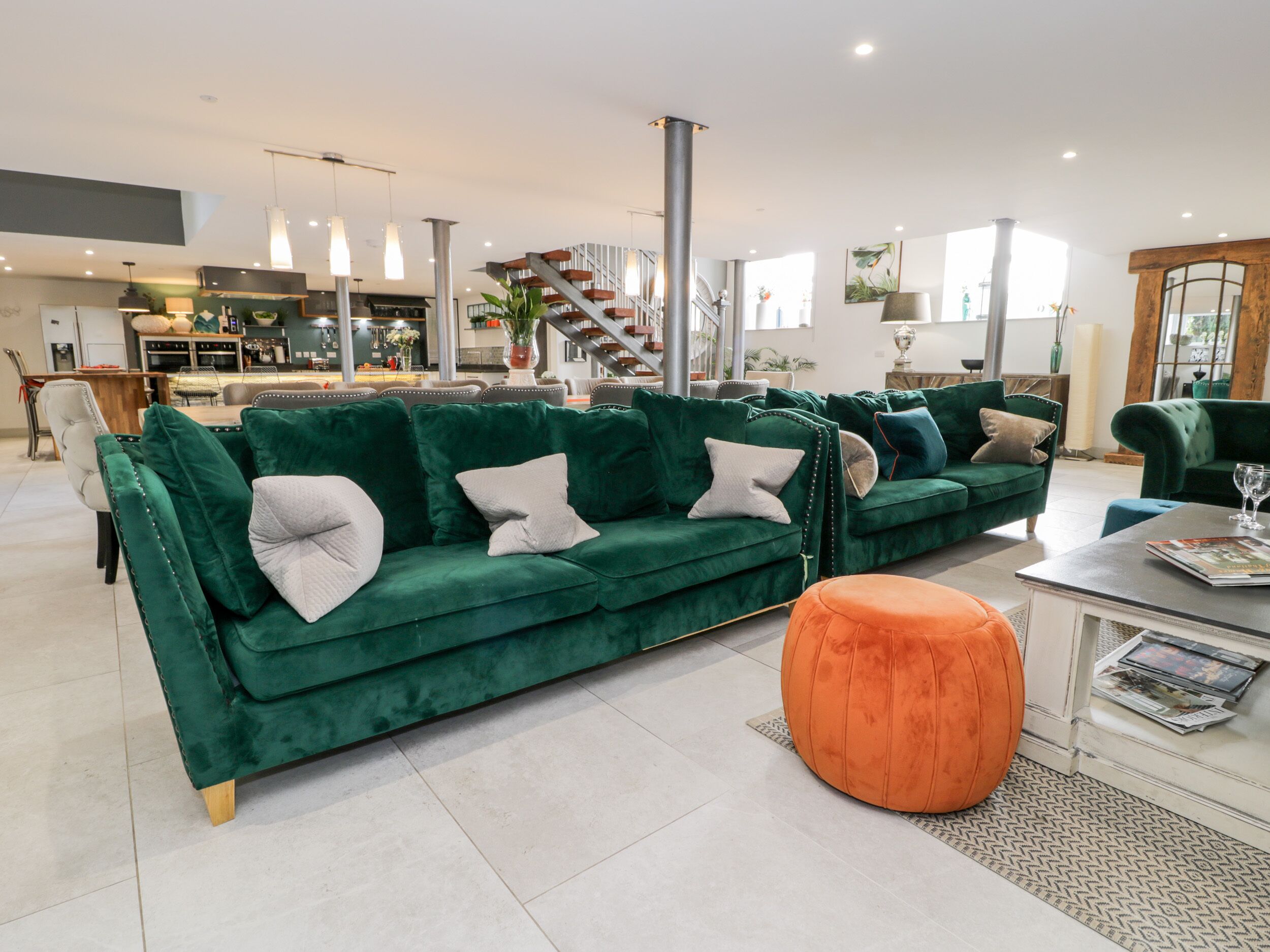 Una sala de estar moderna con un sofá verde, un taburete naranja y un comedor al fondo.