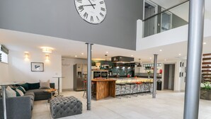 A modern living room with a grey sofa, a grey ottoman, and a dining area with a wooden island and bar stools.