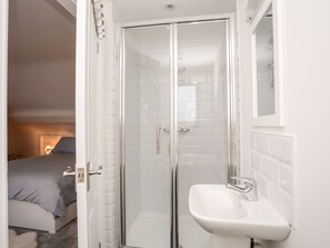 Un baño moderno con cabina de ducha de vidrio, un lavabo blanco y una cama en la habitación contigua.