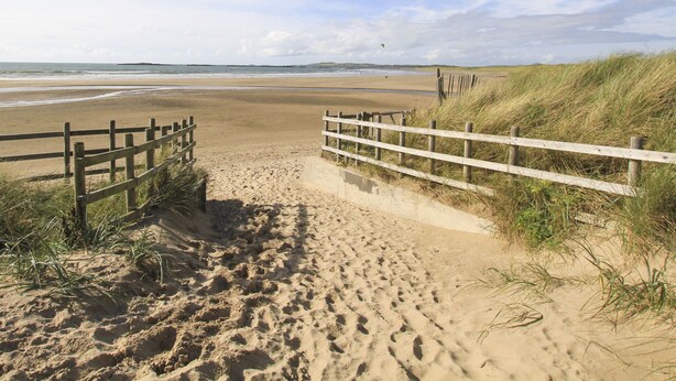 Un sentier de sable qui longe la plage et mène à l’océan, avec des garde-corps en bois de chaque côté.
