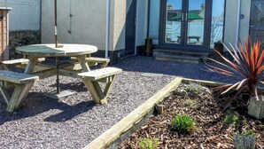Une terrasse avec une table et des bancs en bois, un parasol vert et un jardin avec du paillis et des plantes.