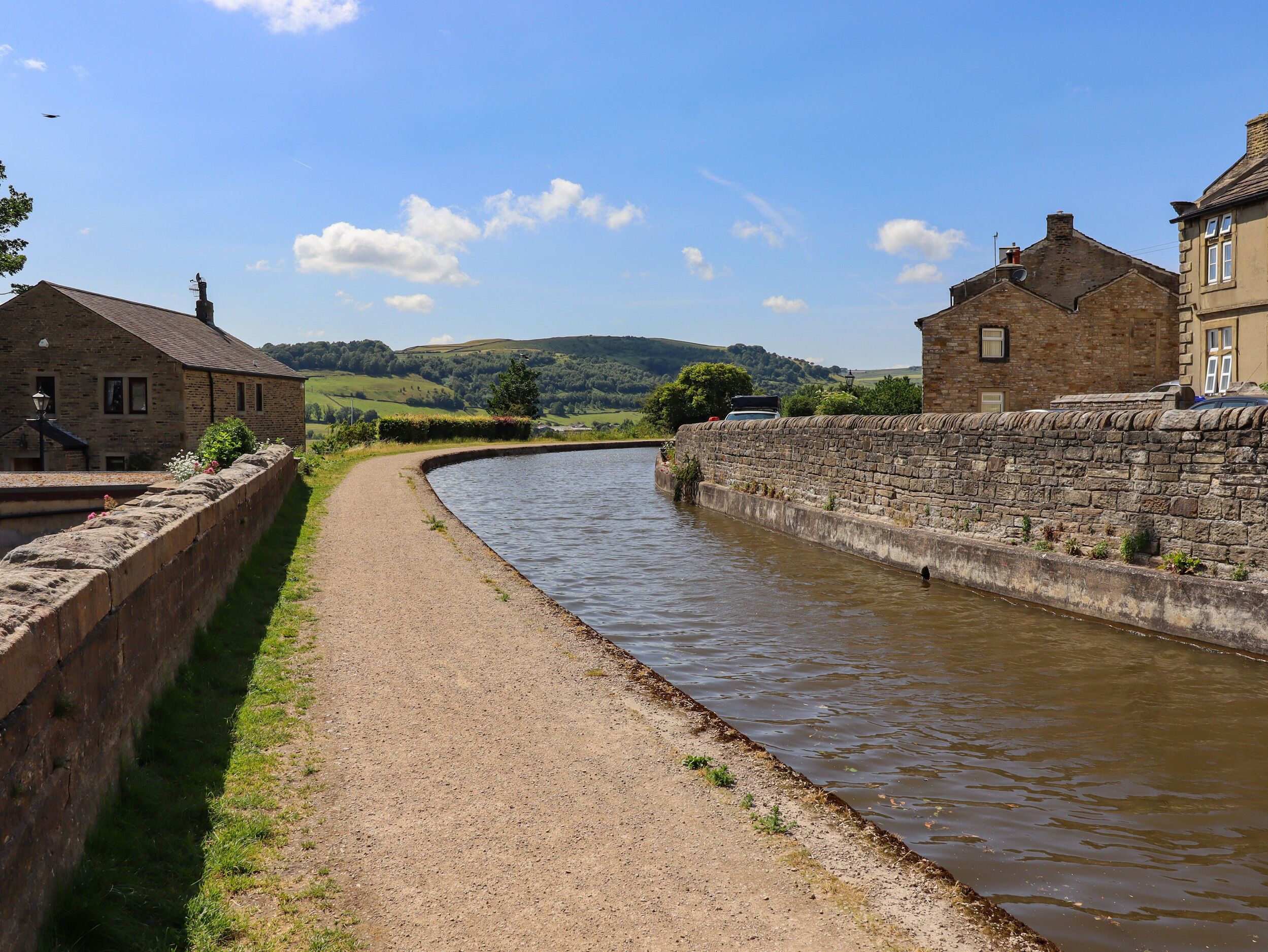 A narrow waterway flanked by stone walls and buildings, with a clear sky and distant hills.