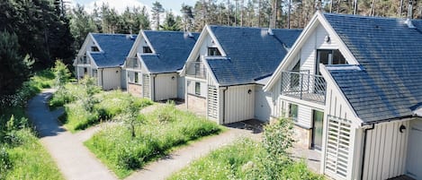 A row of cabins with blue roofs and white walls, surrounded by greenery and a clear sky.
