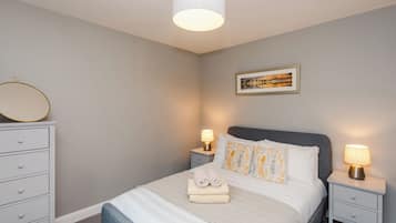 Un dormitorio ordenado con una cama, mesitas de noche, una lámpara, un espejo y un cuadro en la pared.