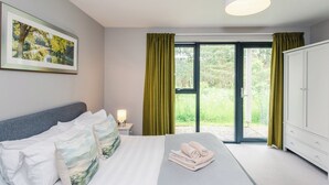 A hotel room with a bed, a nightstand, a lamp, a wardrobe, and a large window with curtains.