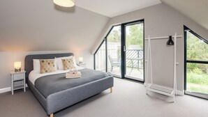 A bedroom with a large bed, a nightstand, a lamp, and a view of the outdoors through a large window.