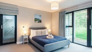 Une chambre à coucher avec un lit, des tables de chevet, un tableau et une vue sur l’extérieur, grâce à une grande fenêtre.
