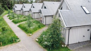 Une rangée de cabanes aux toits inclinés et aux lucarnes, entourées de verdure et bordées d’un chemin de gravier.