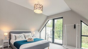 Une chambre moderne avec un grand lit, un luminaire au plafond, une table de chevet et une vue sur l’extérieur grâce à une porte-fenêtre coulissante.