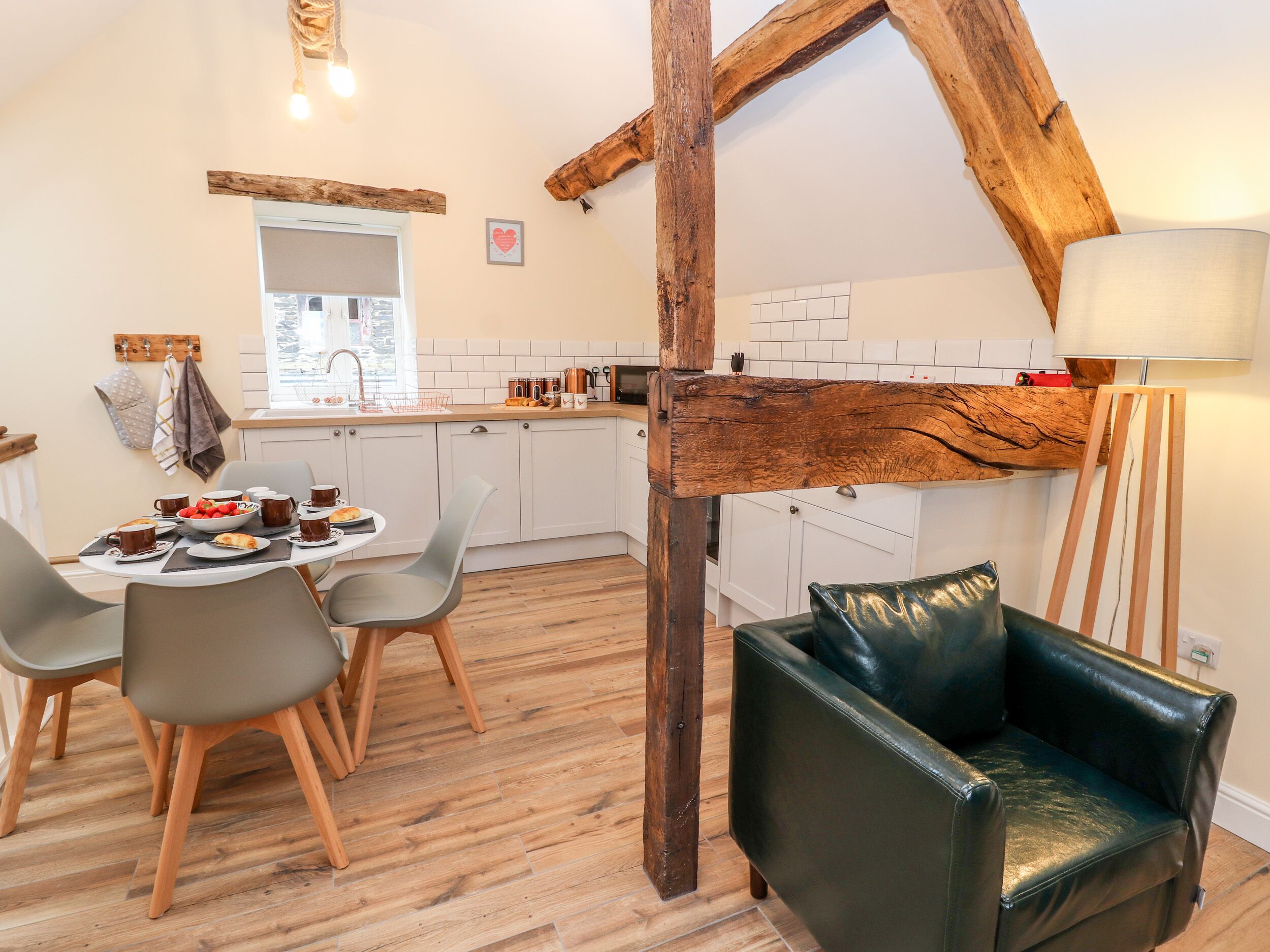 A cozy kitchen with wooden beams, a dining table with chairs, and a leather sofa.