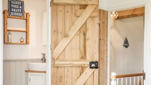 A rustic bathroom with a wooden door, a white sink, and a shelf with toiletries.