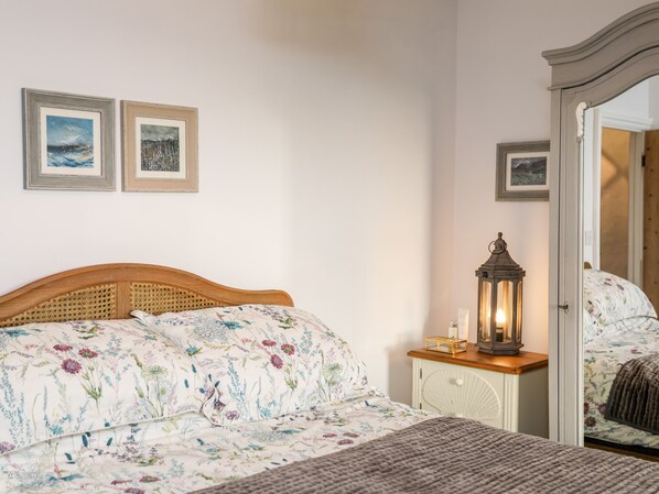 A bedroom with a wooden headboard, floral bedding, a bedside table with a lantern, and two framed pictures on the wall.