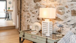A rustic stone wall, a vintage-style lamp, and a decorative shell on a glass table.