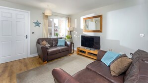 Un salón con un sofá de cuero marrón, un televisor sobre un mueble de madera y una decoración con forma de estrella en la pared.