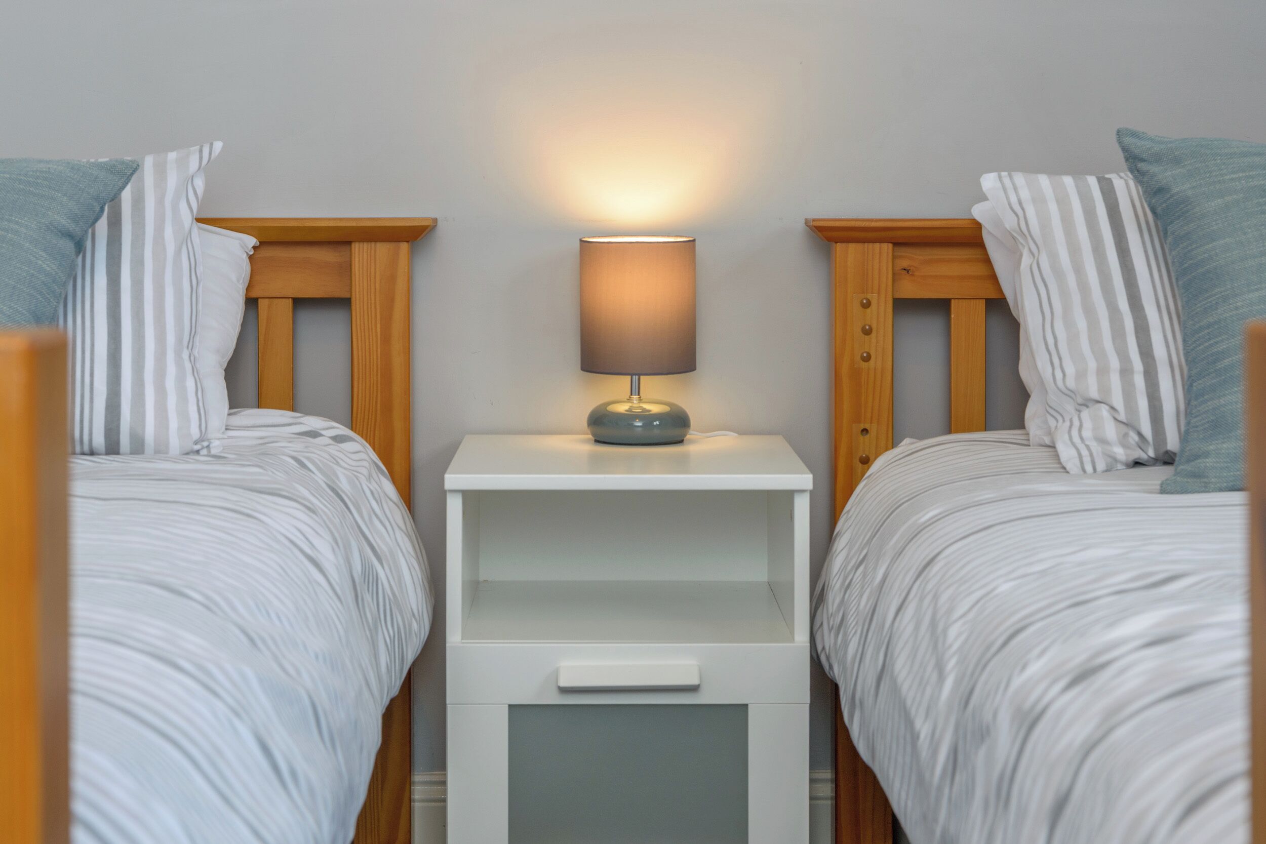 Habitación doble con dos camas, una mesita de noche con lámpara y un cajón.